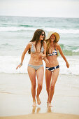 Zwei Frauen in Bikinis und mit Sommerhut an einem Strand