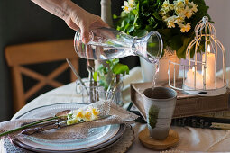 Spring table settings in green colors with Daffodils, female hand pouring water