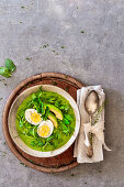 A smoothie bowl with boiled egg, avocado and mange tout in a nest of herbs