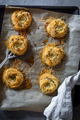 Angel hair pasta nests with pistachios on a baking tray with baking paper and a vintage spatula