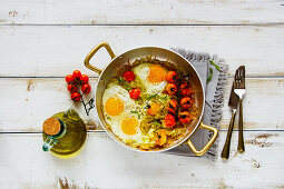 Fried eggs with onion and tomatoes in frying pan on wooden background
