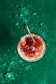 Crushed ice with raspberry syrup in a glass on a green surface