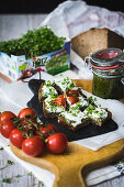 A slice of bread topped with cream cheese, cress and tomatoes with pesto in the background