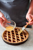 Linzertorte (nut and jam layer cake) being made: lattice pastry being brushed with egg