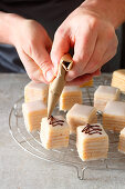 Petit fours being decorated with an egg white glaze and chocolate