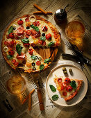 Pizza mit Salami, Schinken, Tomaten, Oliven und Käse auf Tisch