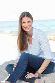 A young woman by the sea wearing a light blue shirt and jeans