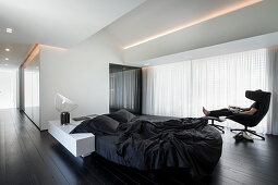 Designer furniture in minimalist, monochrome bedroom; person sitting in lounger