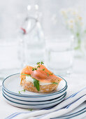 A baguette slice covered with smoked salmon on a stack of plates