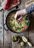 Green curry pasta with limes, herbs and chili pepper in pot on wooden background