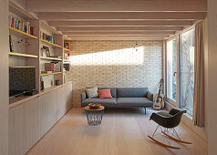 Sofa and shelves in modern living room with brick wall and balcony door