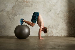 Junger Mann im Handstand, Füsse auf Physioball