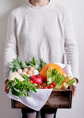 A woman holding a wooden box with a stock of fresh food