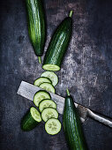 A cucumber, partially sliced, on a grey metal surface