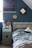 Bedside table and bed with upholstered headboard against blue wall