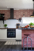 Island with dusky-pink wooden front and vintage-style wallpaper above kitchen counter