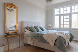 Gilt-framed mirror next to bed in elegant bedroom in period building