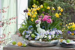 Silver bowl with daffodils, ranunculus, checkerboard flowers, violets and grape hyacinths, Easter bunny and Easter eggs as decoration