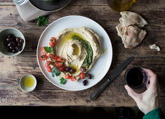 Hand dipping piece of fresh flatbread into tasty hummus pesto, decorated with cherry tomatoes and beans with parsley