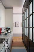 Narrow kitchen separated by black lattice and glass partition