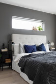 Doppelbett mit gepolstertem Kopfteil in Schlafzimmer mit dunkelgrauen Wänden