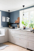 White kitchen counter with marble worksurface below window in kitchen with grey-blue walls