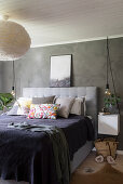 Collection of scatter cushions on double bed and lamp with fluffy lampshade in bedroom with grey walls