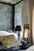 Decorative, sequinned scatter cushion on four-poster bed against partition wall