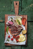 A grilled club steak with vegetables on a chopping board