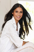 A dark-haired woman wearing a white shirt-blouse and white trousers