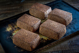 Square loaves of rye bread with flax seeds on a baking tray