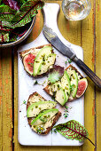 Slices of bread topped with avocado, figs, pistachio nuts, thyme and wild herb salad