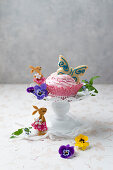 A cupcake with strawberry cream and butterfly biscuits, tufted pansies and forget-me-nots