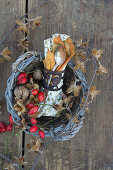 A napkin and cutlery in a basket decorated with rosehips, walnuts and beehnuts