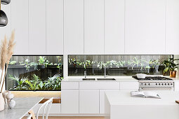 Offene moderne weiße Küche mit Pflanzenterrarium als Küchenrückwand