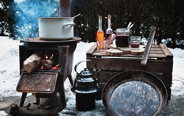 A winter barbecue with a rustic wood-fired oven and utensils in the snow