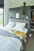 Bed with grey-upholstered headboard against partition wall screening walk-in wardrobe