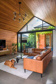 Brown leather corner couch in living room with wooden walls and wooden pointed roof