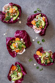 Healthy eatable radicchio bowls with couscous, avocado, dates. carrots, cucumber, herbs and sesame seeds