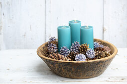 Blaue Stumpenkerzen in Schale mit verzierten Zapfen als edle Weihnachtsdeko