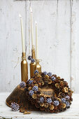 Bottles sprayed gold and used as candlesticks behind handmade wreath of pine cones