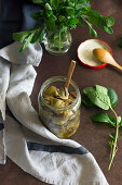 Jar of yummy marinated artichokes with basil leaves placed on brown table near napkin