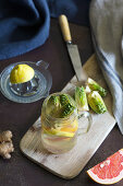 Jar of fresh citrus beverage with fresh artichoke and ginger placed on wooden board