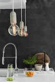 Light bulb pendant lamps above kitchen worksurface against charcoal-grey wall