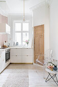 White fitted kitchen with stucco ceiling, board floor, side table and classic chair