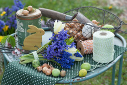 Easter decoration with a bouquet of hyacinth, grape hyacinth and tulips, wooden Easter bunny, Easter eggs, basket with onions, string