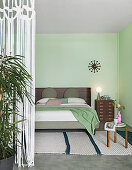 Double bed and pale green walls in sleeping area separated by string curtain in loft apartment