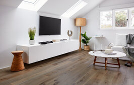 Wohnzimmer mit Lowboard, Fernseher an der Wand, Stehleuchte, Sofa und Coffeetable im Dachzimmer