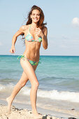 A brunette woman by the sea wearing a colourful bikini