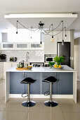 Kitchen counter, bar stools, pendant lamps and shiny tiled floor in open-plan kitchen